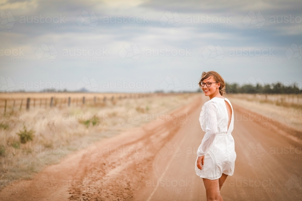 Young woman in white walking barefoot on rural dirt road - Australian Stock Image
