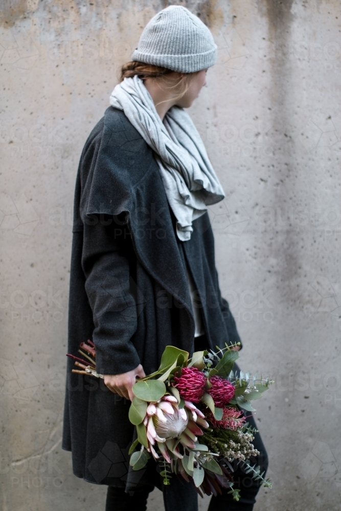 Young woman in winter clothing turning away from camera holding a native floral bouquet - Australian Stock Image