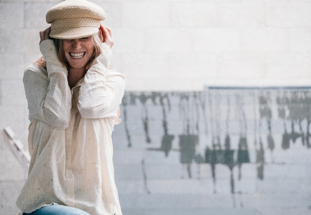 Young woman laughing as she pulls on a cap. - Australian Stock Image