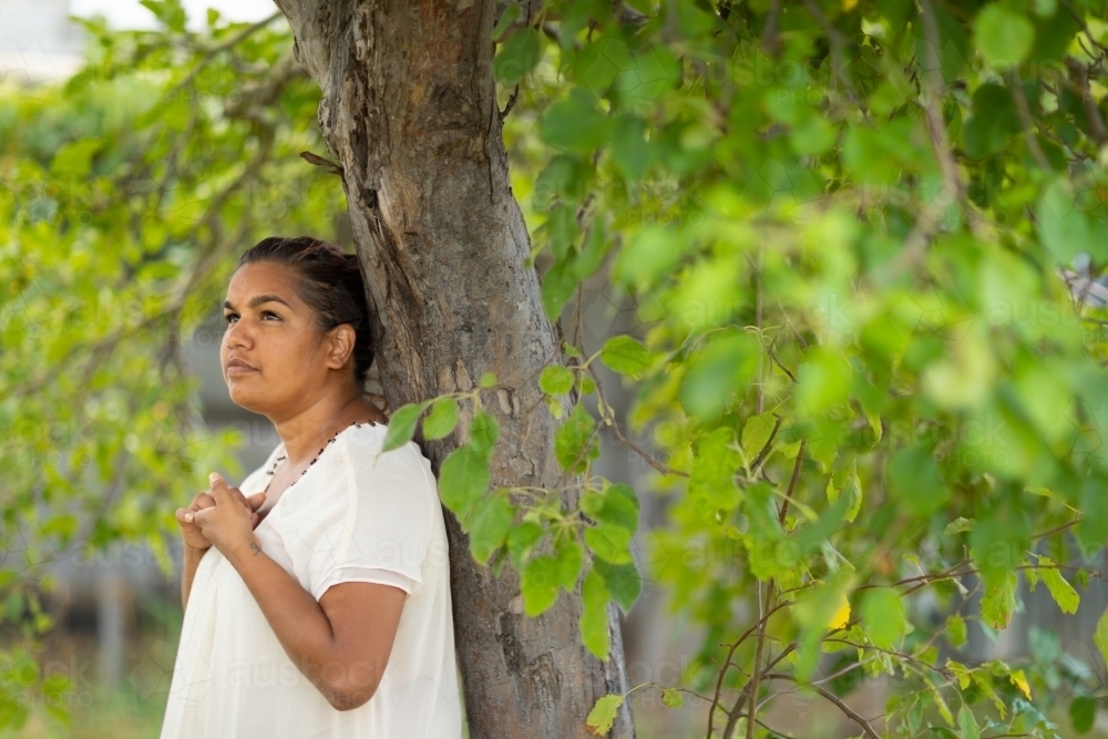 young woman leaning against tree in contemplation - Australian Stock Image