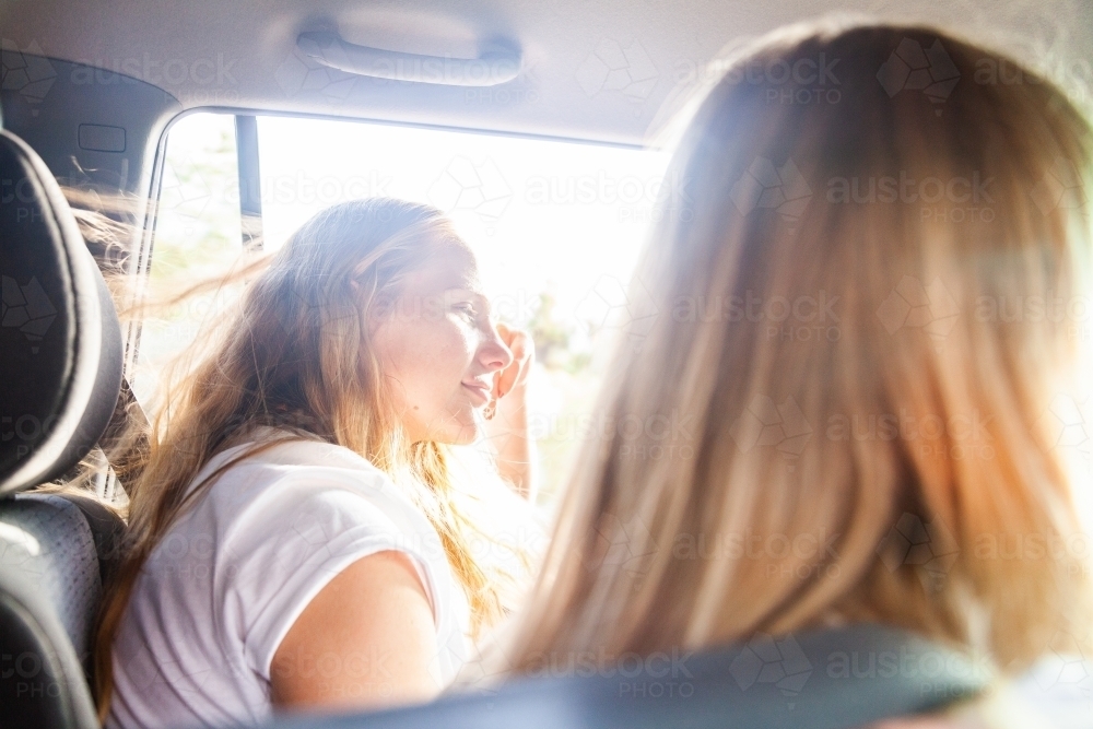 Young woman leaning out car window smiling on road trip with friends - Australian Stock Image