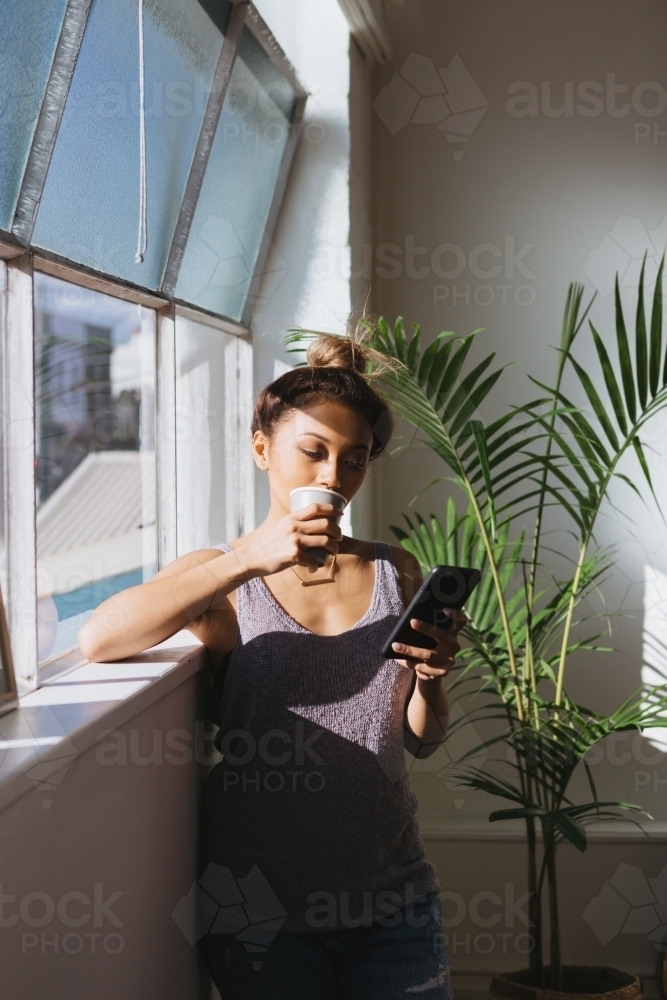 Young woman looking at her mobile phone with a coffee - Australian Stock Image