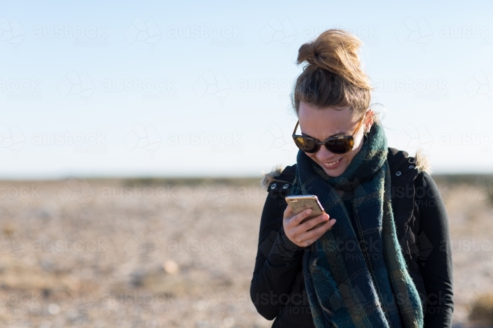 Young woman looking at smartphone in arid landscape - Australian Stock Image