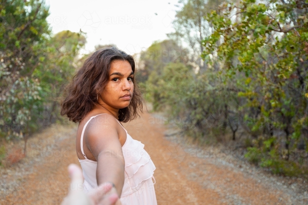 young woman looking back towards first person viewer with arm outstretched - Australian Stock Image