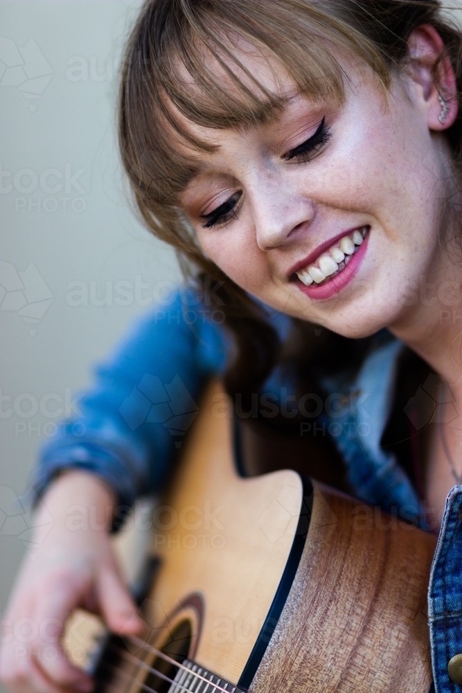 Young woman looking down playing guitar outside - Australian Stock Image
