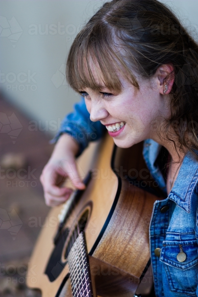 Young woman looking down playing guitar outside - Australian Stock Image