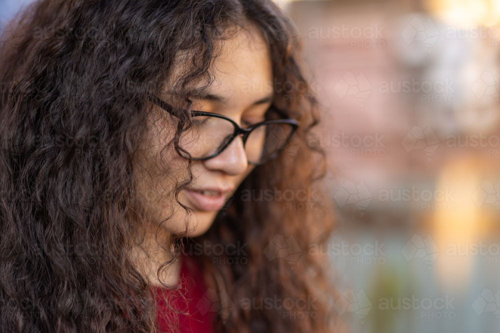 young woman looking down through glasses with long dark curly hair falling over her face - Australian Stock Image