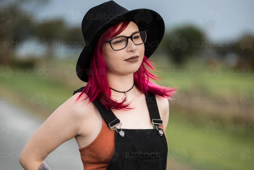 Young woman looking off with pink hair hat and glasses - Australian Stock Image