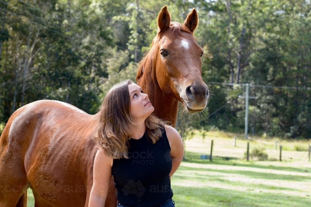 Young woman looking up affectionately at a chestnut horse - Australian Stock Image