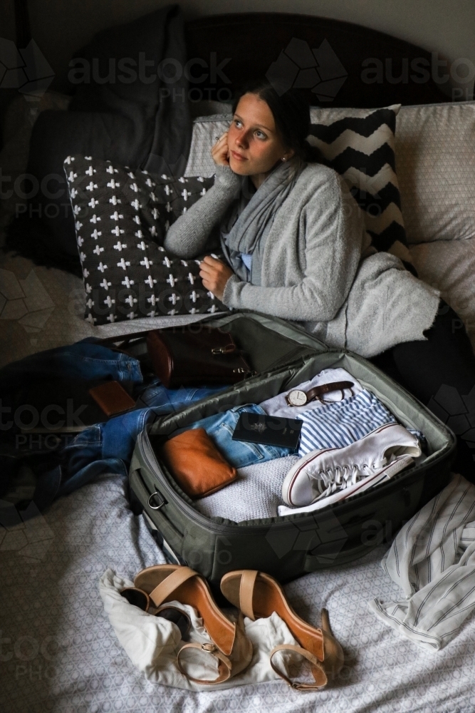 Young woman lying on her bed beside her bag packed and ready to travel - Australian Stock Image