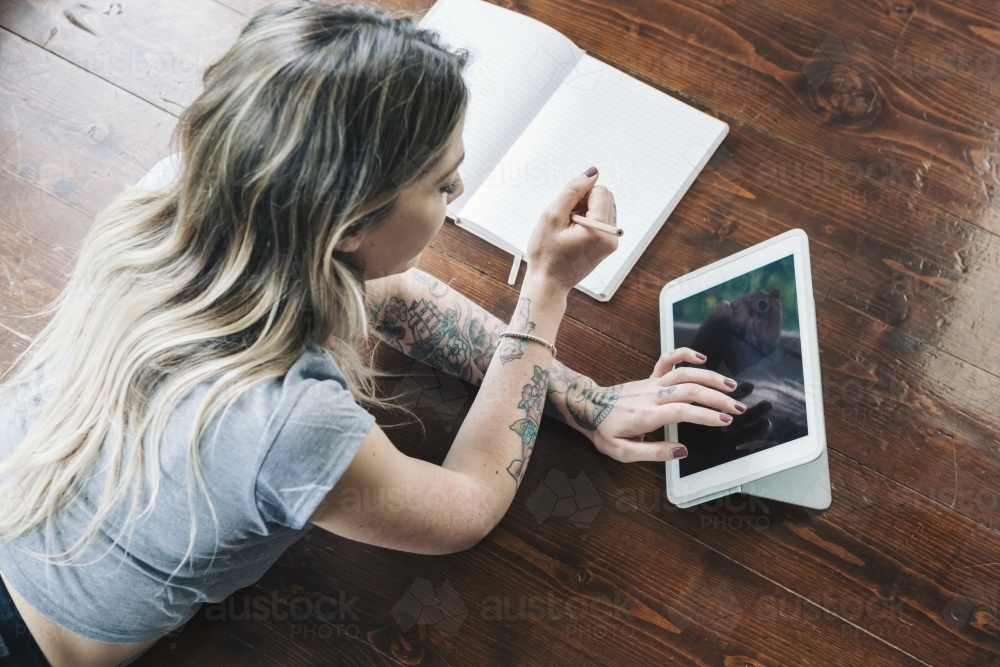 Young woman lying on the floor studying and browsing the internet on a tablet - Australian Stock Image