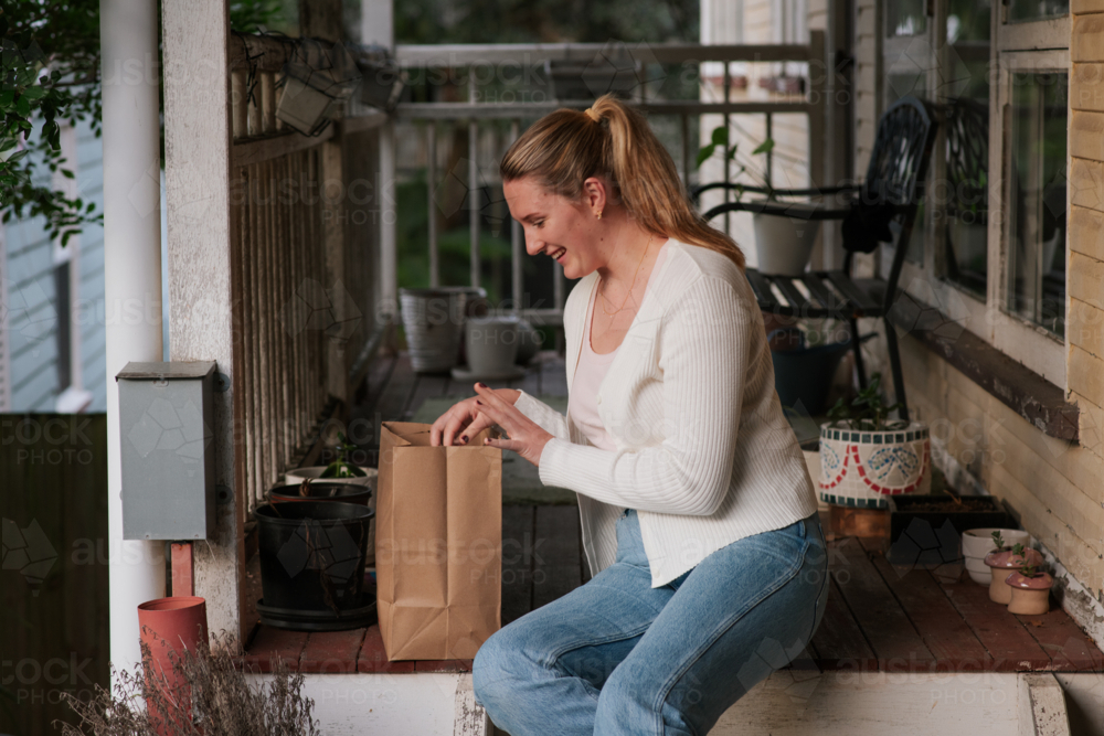 Image of young woman on a wooden porch, with grocery bag - Austockphoto
