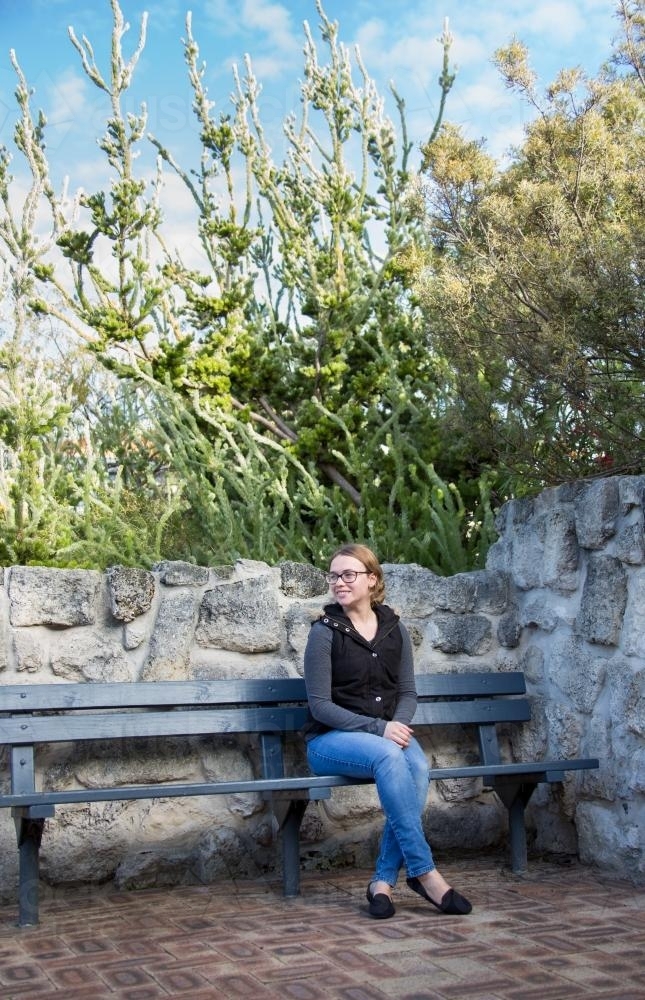 Young woman on bench near stone wall - Australian Stock Image