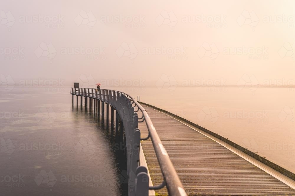 Young woman on curved jetty in the rain - Australian Stock Image