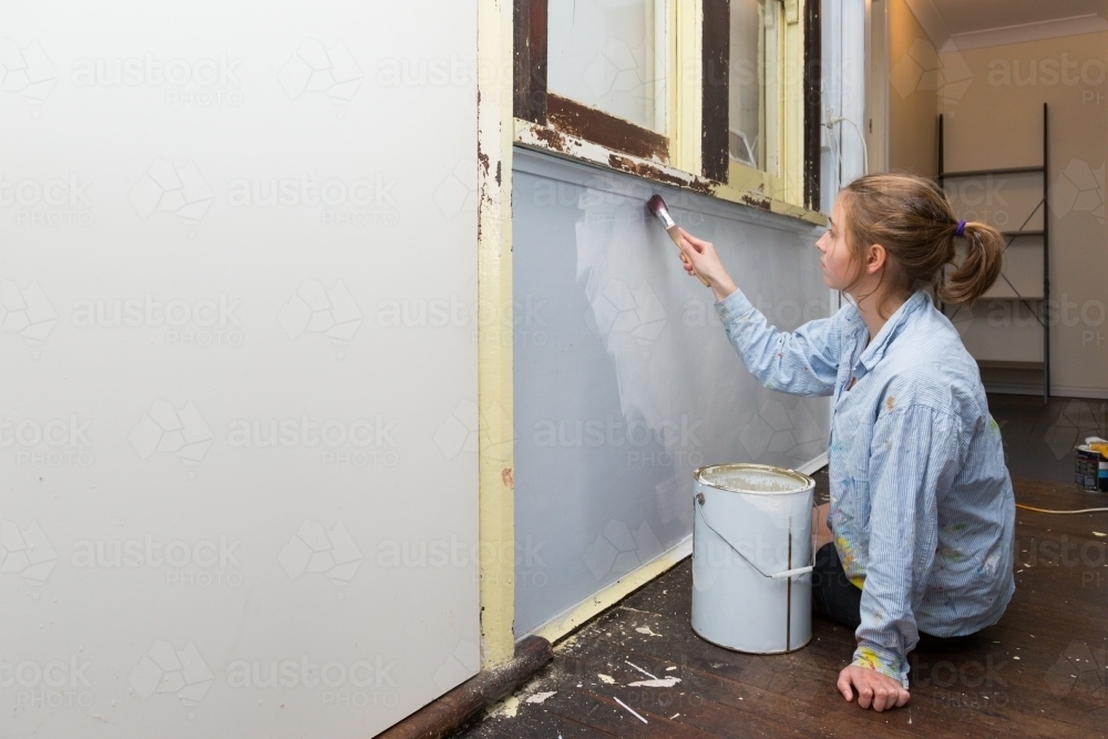 Young woman painting interior wall in old house - Australian Stock Image