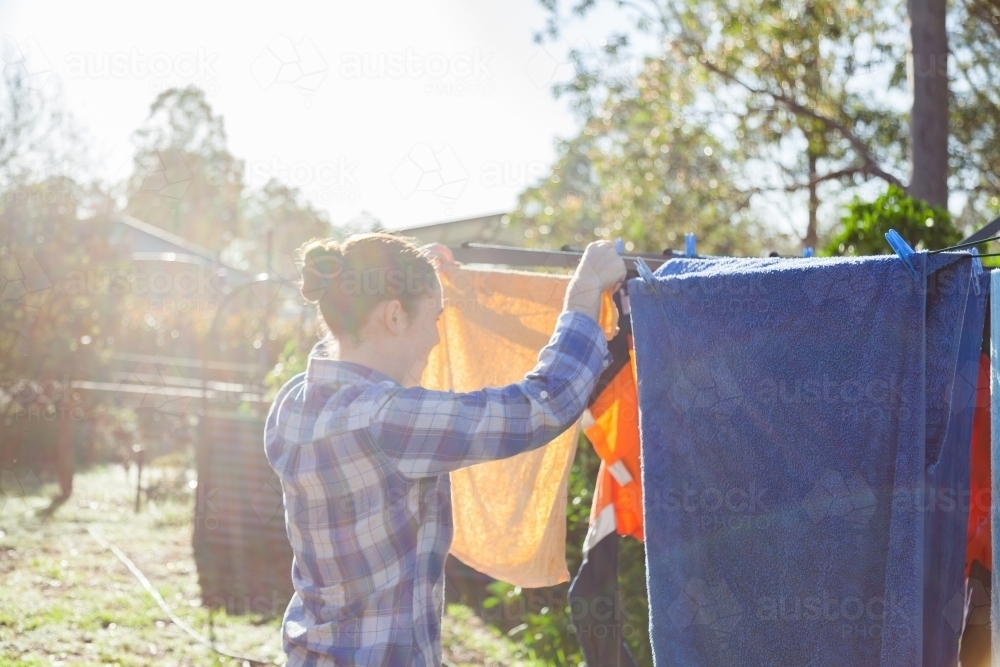 Young woman pegging clothes to washing line in backyard - Australian Stock Image