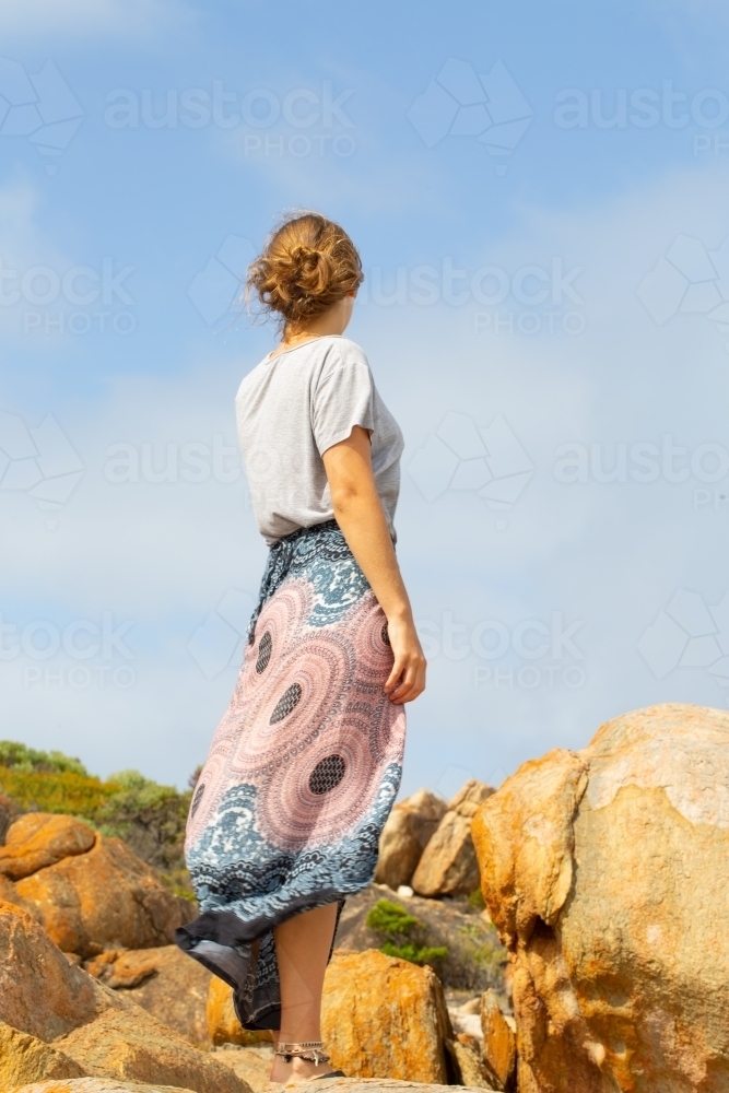 Young woman photographed from behind against rocks and sky - Australian Stock Image