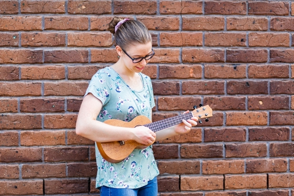Young woman playing a ukulele near brick wall busking - Australian Stock Image