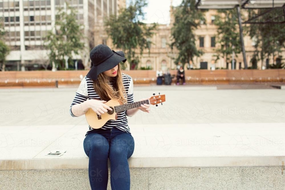 Young woman playing a ukulele on city street - Australian Stock Image
