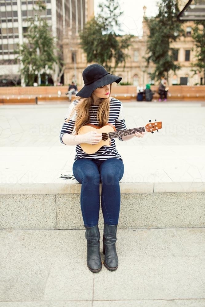 Young woman playing a ukulele on city street - Australian Stock Image