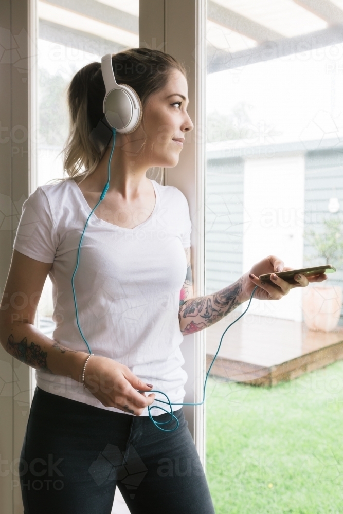 Young woman playing music on her phone looking out the window - Australian Stock Image
