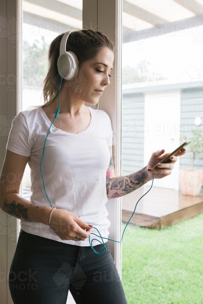 Young woman playing music on her phone with headphones at home - Australian Stock Image