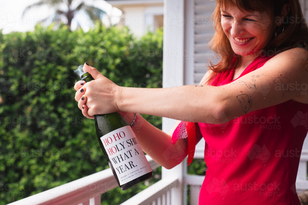 young woman popping open a bottle of champagne - Australian Stock Image