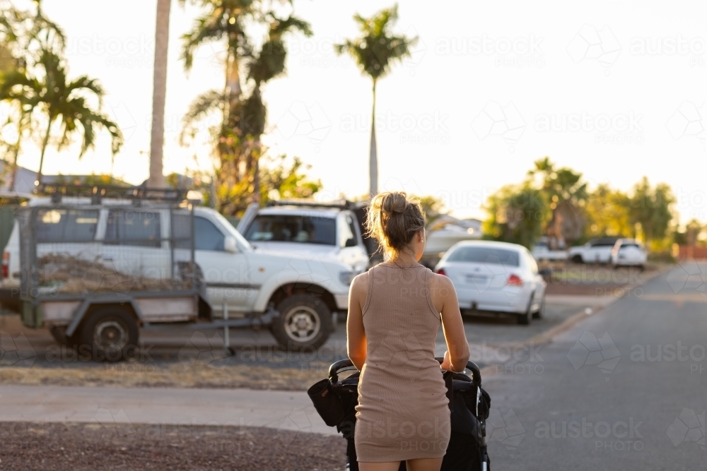 young woman pushing pram along edge of street - Australian Stock Image