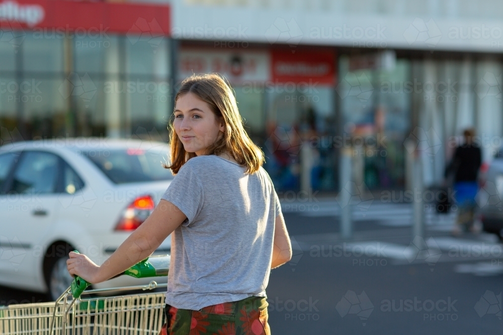 young woman pushing shopping trolley looking over her shoulder - Australian Stock Image