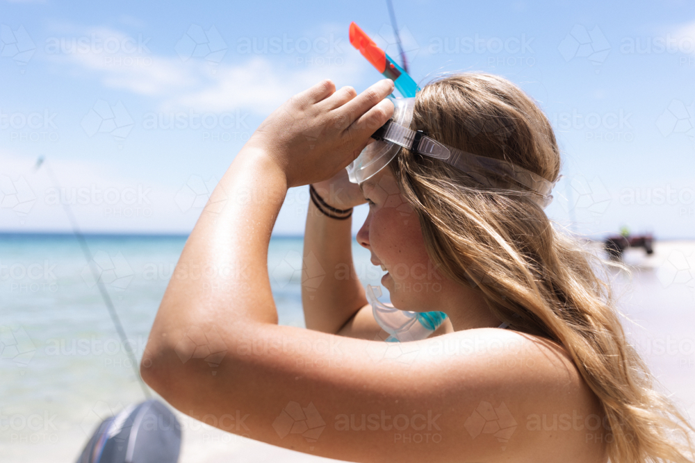 Young woman putting on snorkelling mask at the beach with boat in background - Australian Stock Image