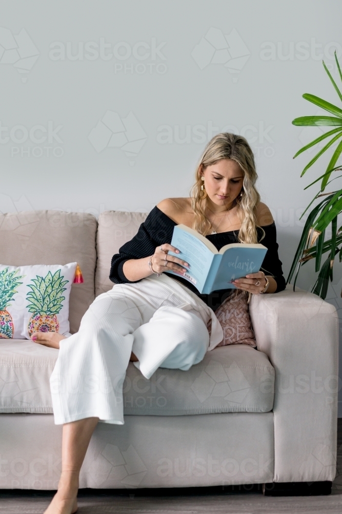 young woman reading a book at home on lounge - Australian Stock Image