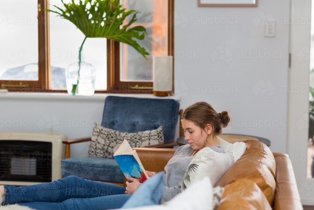 Young woman relaxing at home reading a book - Australian Stock Image