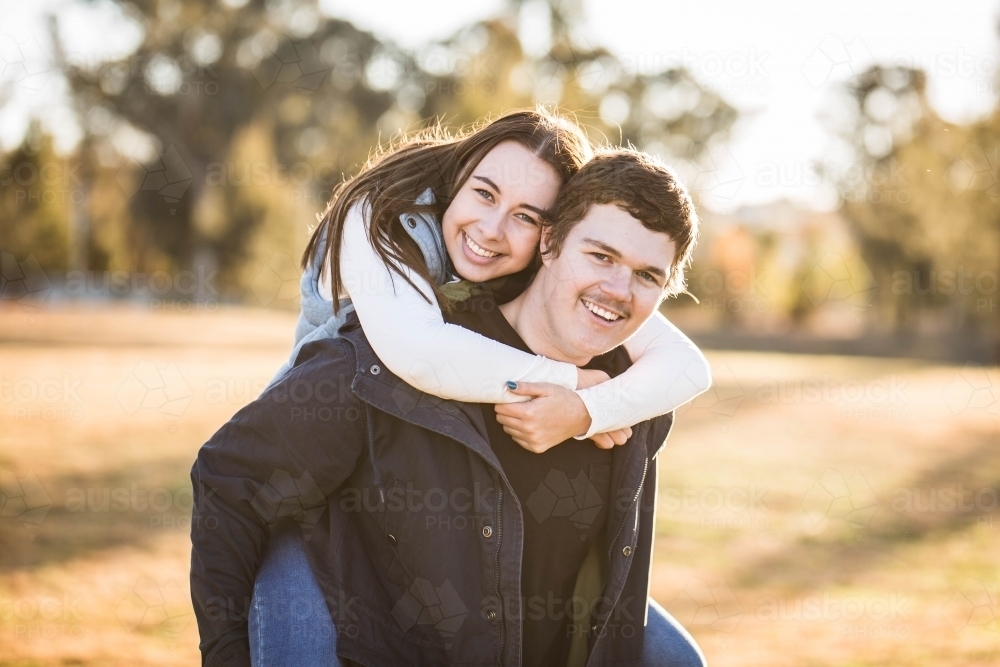 Young woman riding piggy back on boyfriend smiling - Australian Stock Image