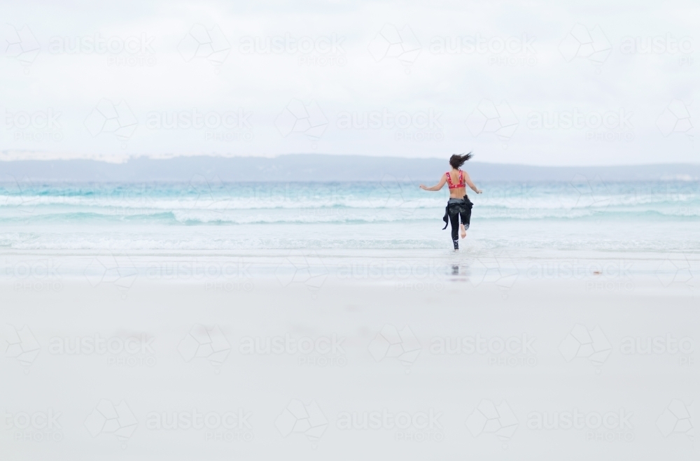 Young woman running down to the water on the beach - Australian Stock Image