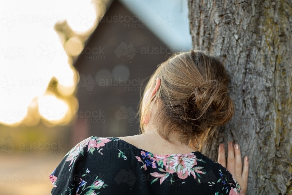 young woman seen from behind leaning head against tree - Australian Stock Image