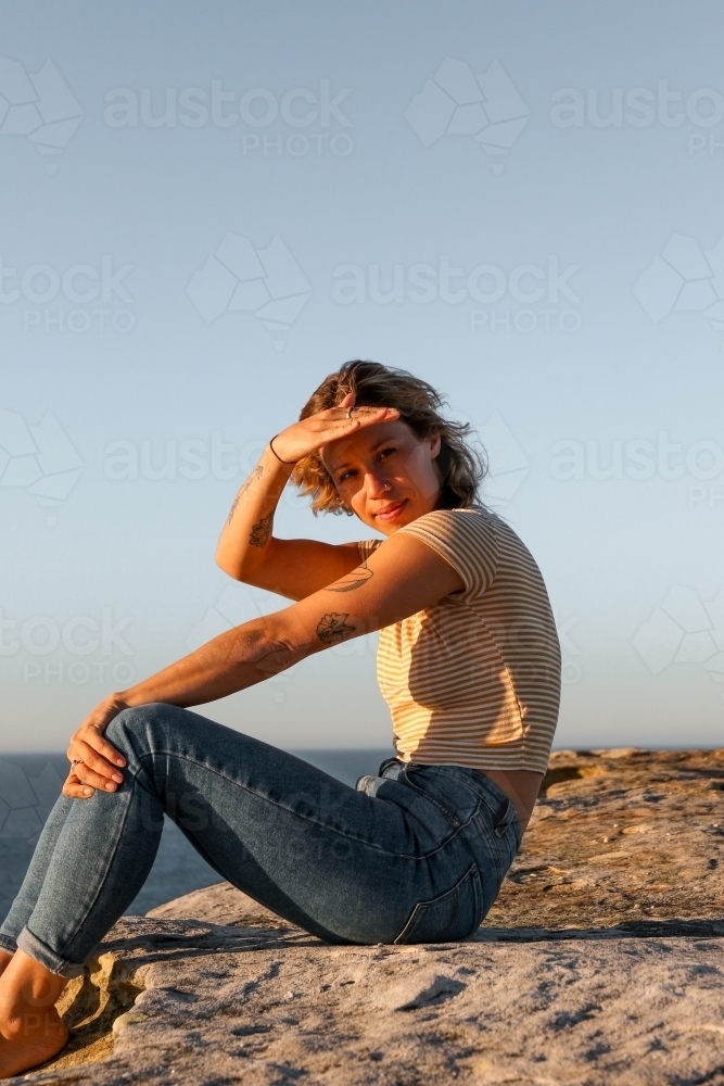 Young woman shielding her eyes from morning sunlight on coastal clifftop - Australian Stock Image