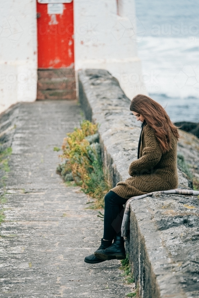 Young woman sits alone out by the lighthouse. - Australian Stock Image