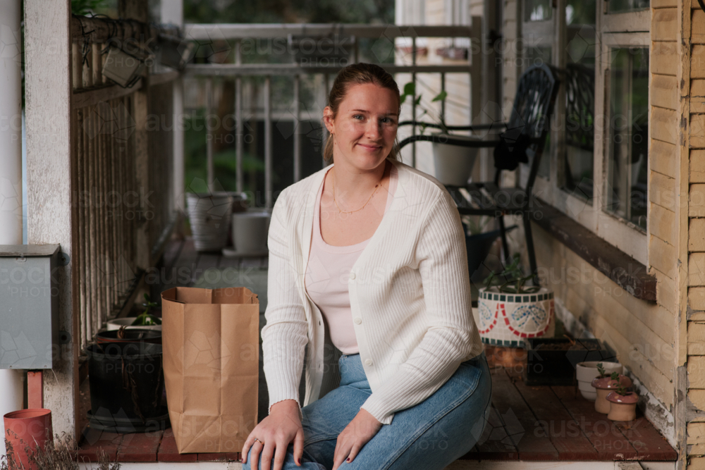 Image of young woman sits casually on a wooden porch, with a paper ...