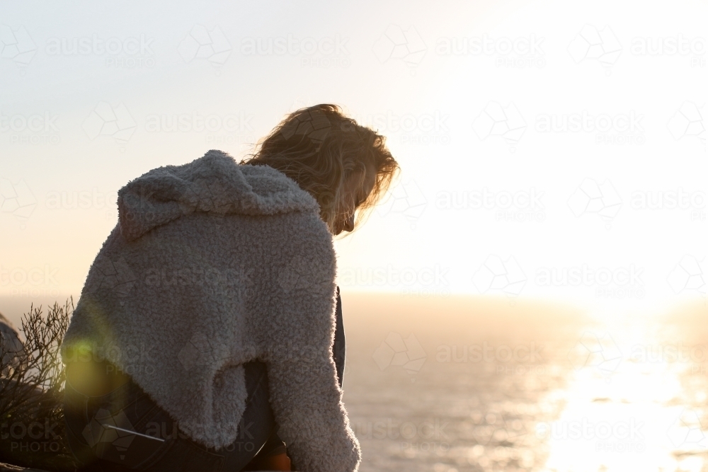 Young woman sitting above ocean at sunrise - Australian Stock Image
