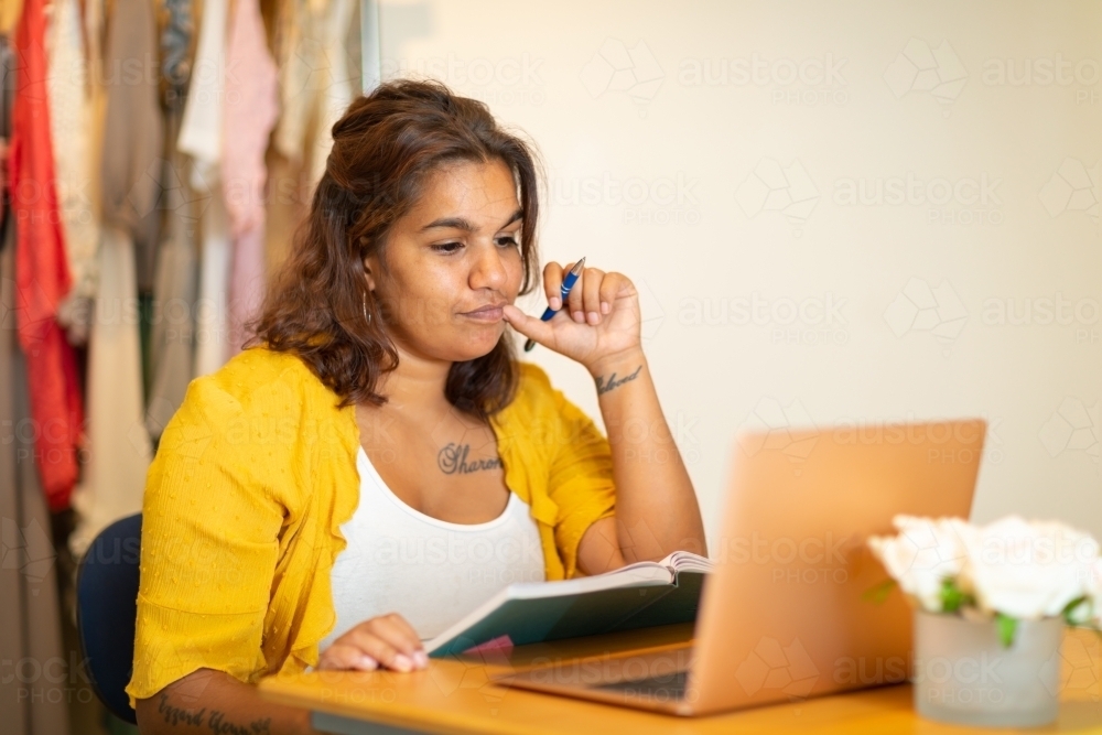 young woman sitting at desk consulting her laptop and diary - Australian Stock Image