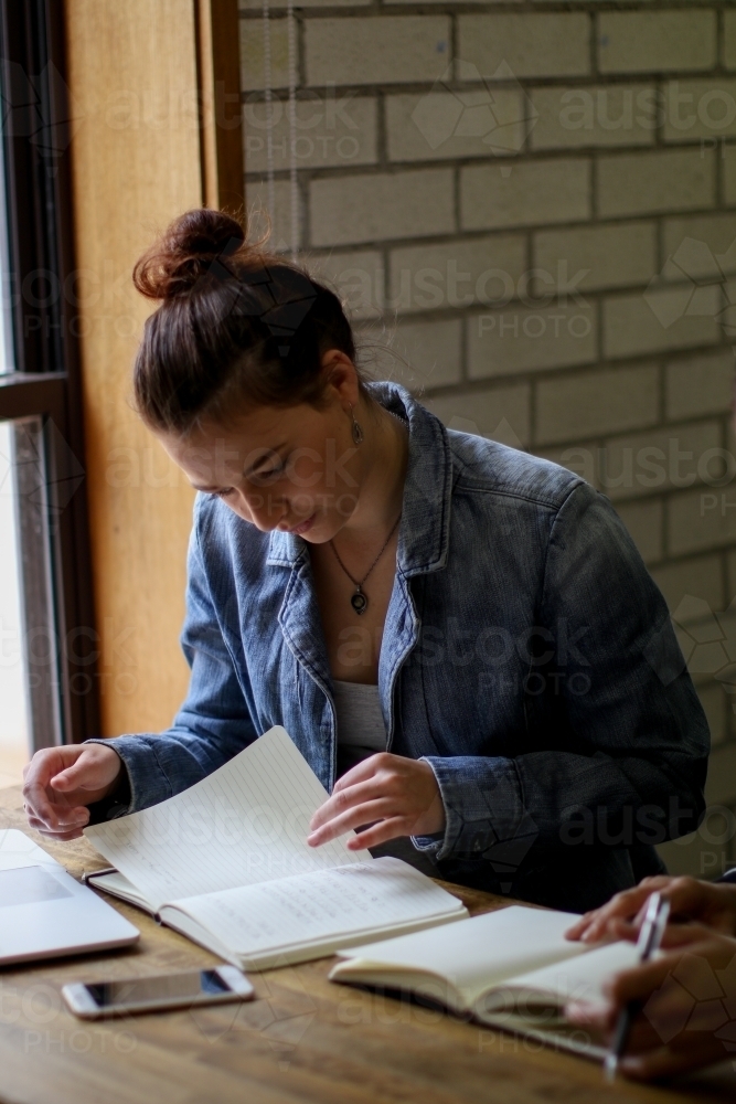 Young woman sitting at desk studying with books and laptop - Australian Stock Image