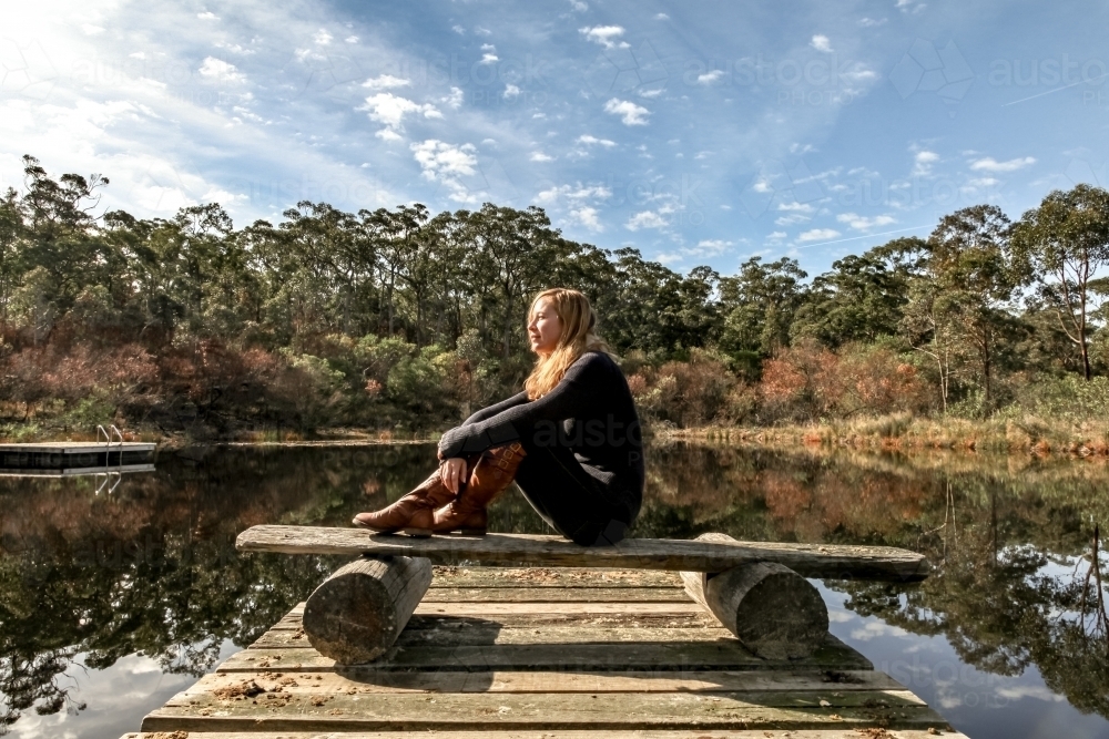Young woman sitting by a lake on a sunny day - Australian Stock Image