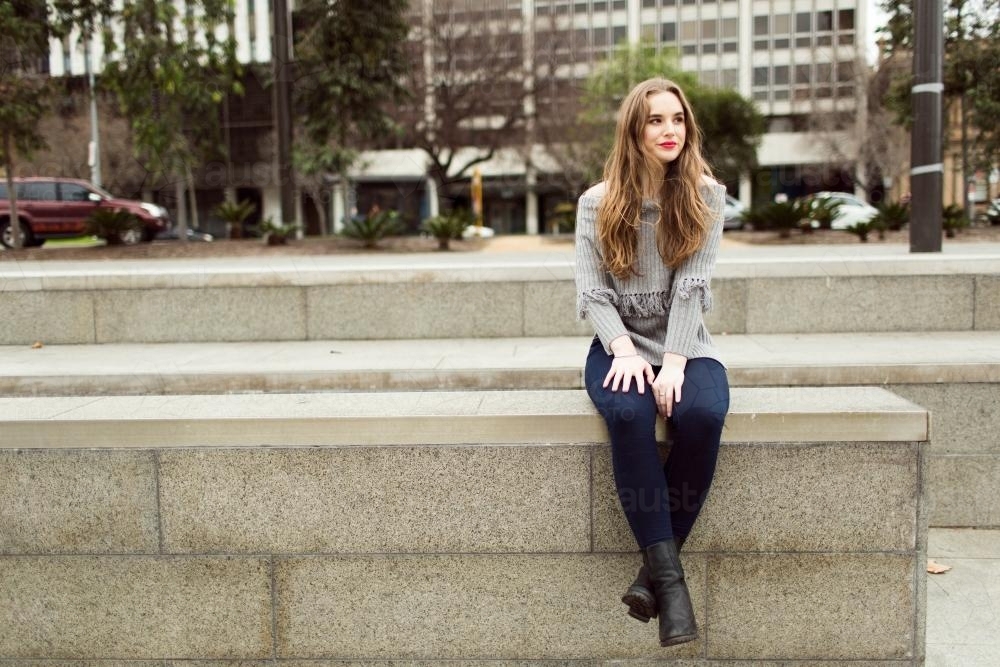 Young woman sitting down on wall in the city - Australian Stock Image
