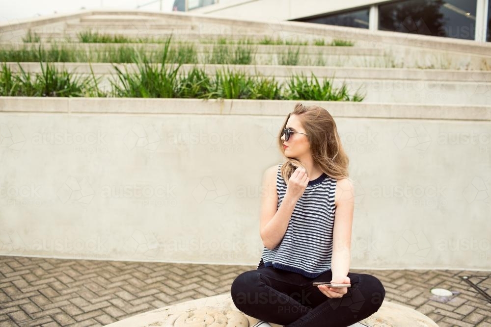 Young woman sitting down with phone and sunglasses - Australian Stock Image