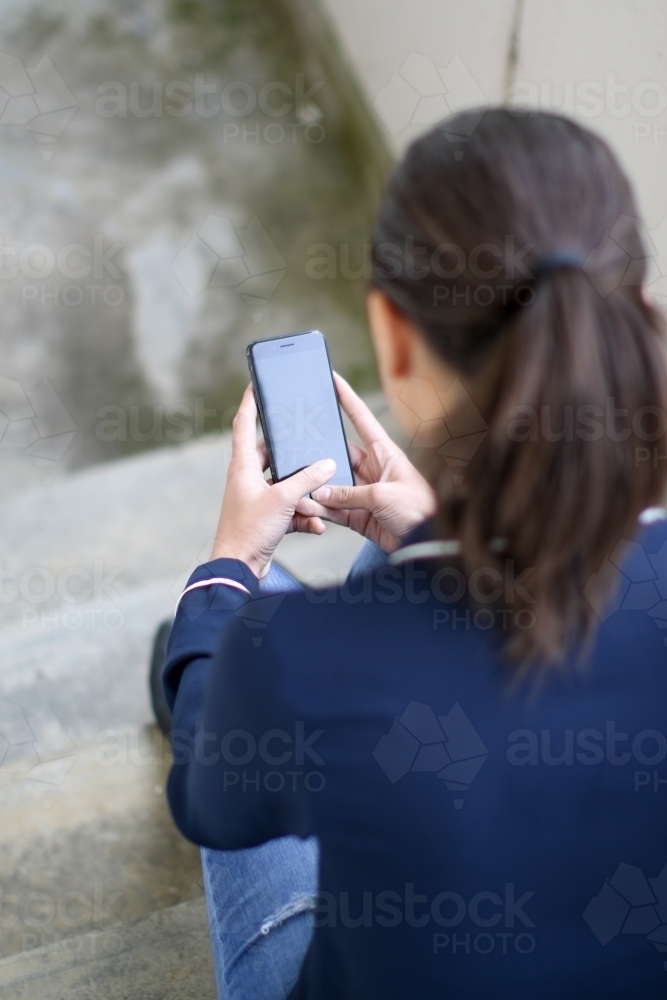 Young woman sitting in stairwell using mobile phone - Australian Stock Image