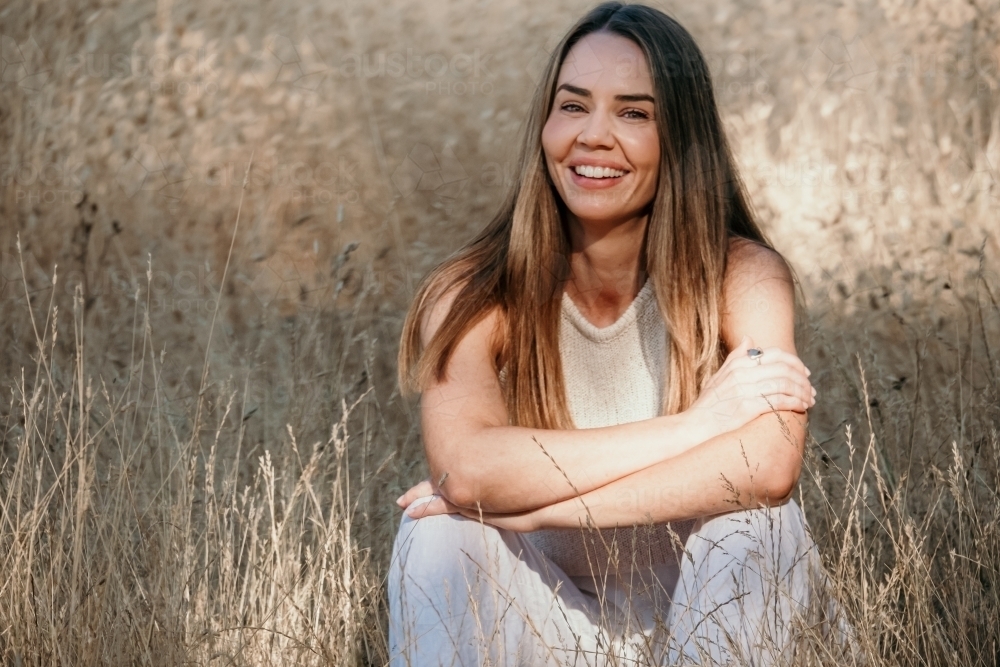 Young woman sitting in the grass smiles. - Australian Stock Image