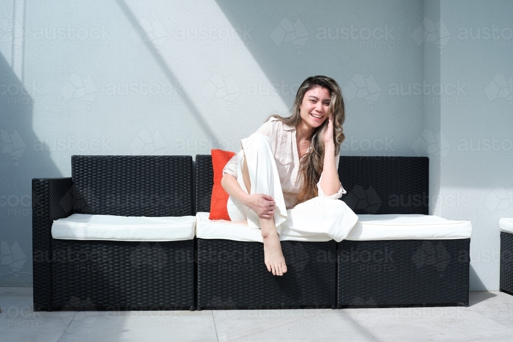 Young woman sitting on an outdoor chair happily posing on a sunny day - Australian Stock Image