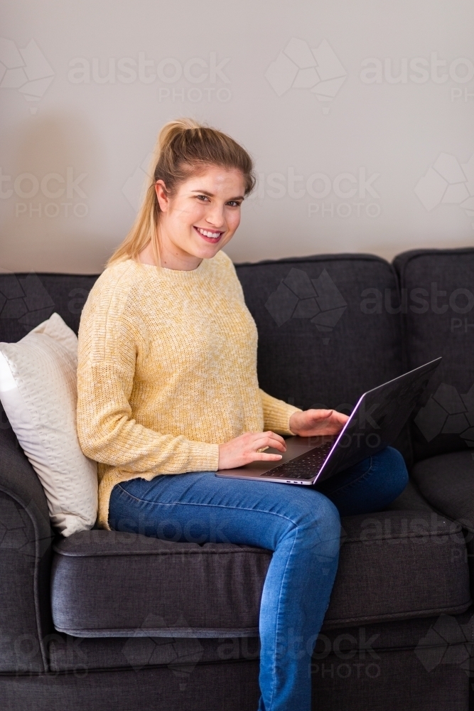 Young woman sitting on lounge working from home on the laptop - Australian Stock Image