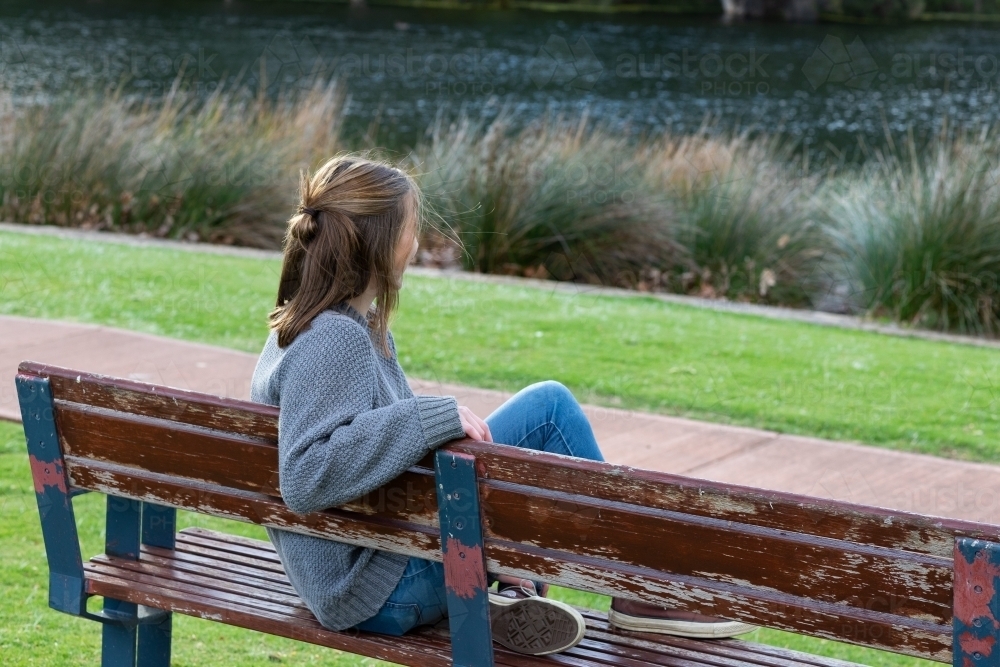 young woman sitting on park bench looking away from camera - Australian Stock Image