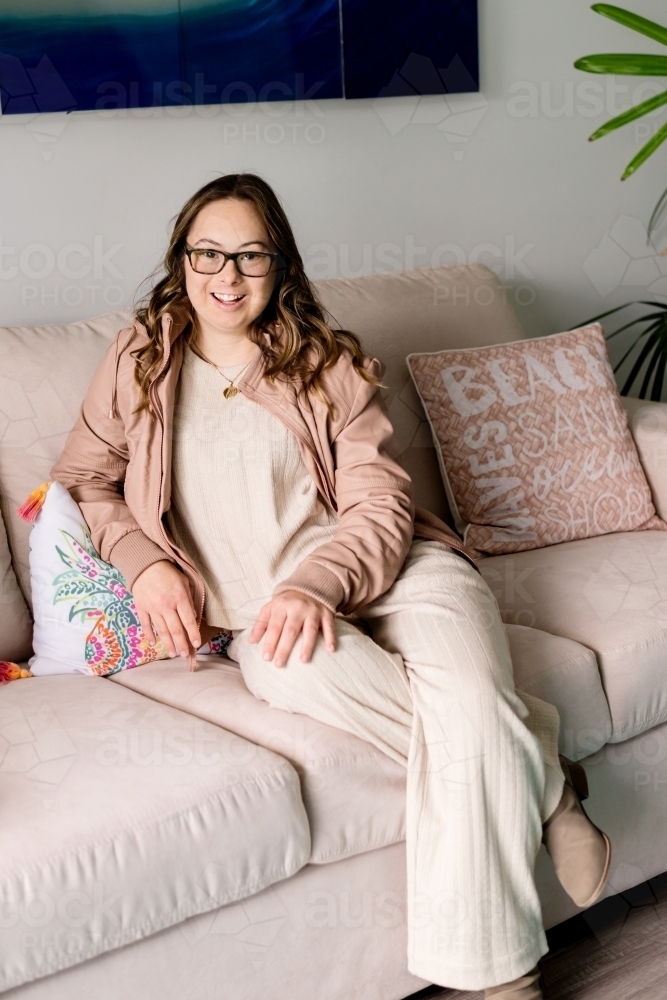 young woman sitting on sofa, from a series featuring a woman with Down Syndrome - Australian Stock Image